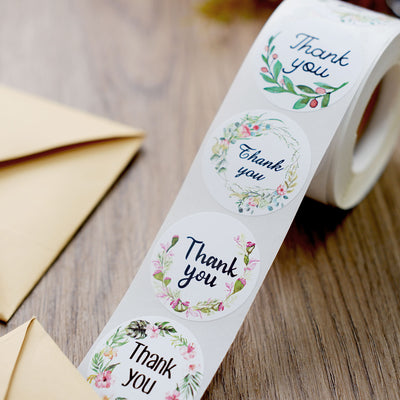 Floral thank you sticker roll on a wooden surface.