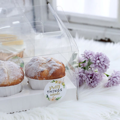 Two freshly baked muffins in a clear container with a flower backdrop.