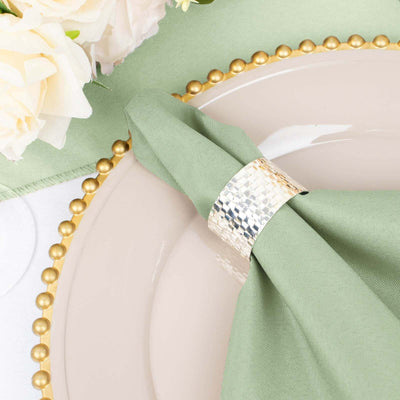 Green napkin with a silver napkin ring on a decorative plate.