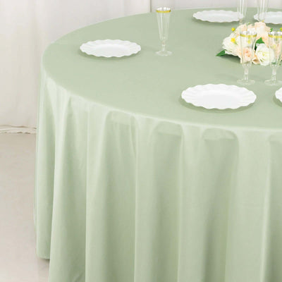 Round mint green tablecloth draping over a table set with white plates and glasses.