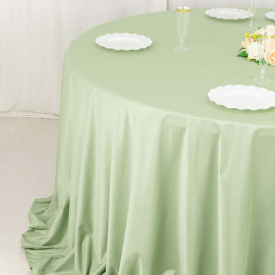 Green tablecloth draped over a round table with white plates and floral centerpiece.