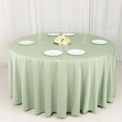 Round green tablecloth draped over a circular table with white plates and floral centerpiece.