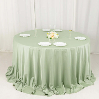 Round green tablecloth draped on a circular table with white plates and floral centerpiece.