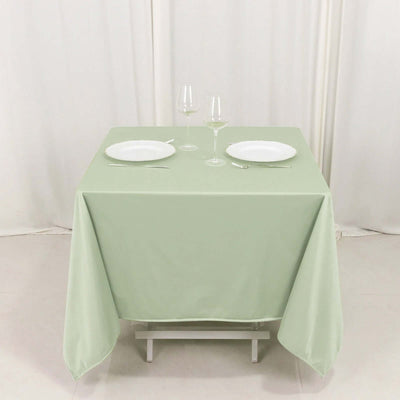Table set with green tablecloth, plates, and glasses on a plain backdrop.