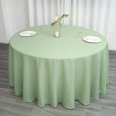 Round green tablecloth draped over a table with plates and decor.