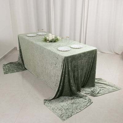 Elegant green velvet tablecloth draped on a table with white plates and candles.