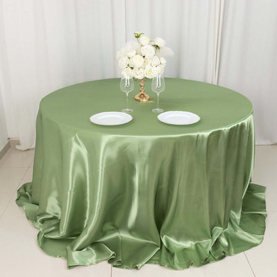 Round green satin tablecloth with white plates and floral centerpiece.