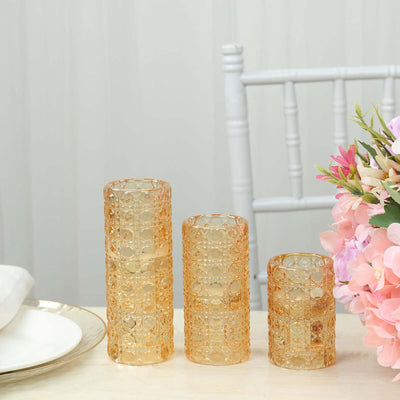 Set of three elegant amber glass vases on a table with flowers.