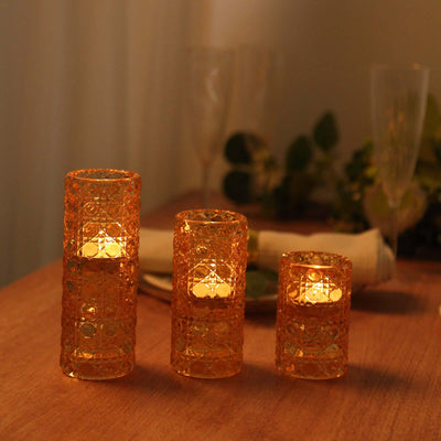 Set of three decorative orange candle holders glowing warmly on a wooden table.