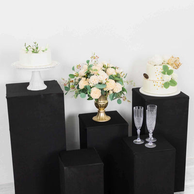 Elegant floral arrangement with cakes and champagne glasses on black pedestals.