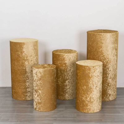 Set of five golden velvet pedestals in varying heights and sizes.