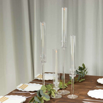 Elegant clear candle holders on a wooden table with greenery accents.