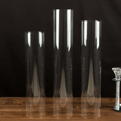 Set of three clear glass vases in varying heights on wooden surface.