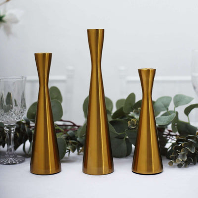 Gold metal vases in varying heights on a table with greenery.