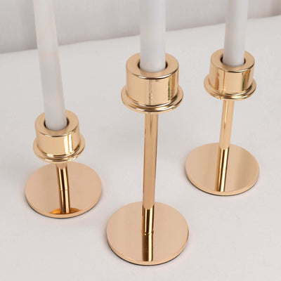 Gold candle holders with white candles on a plain backdrop.