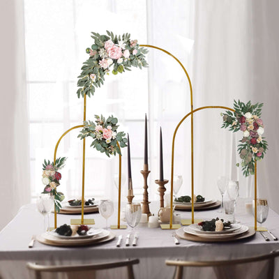 Elegant floral table centerpiece with gold arches and candles for dining.