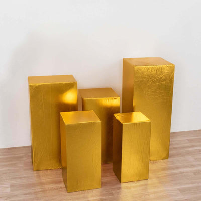 Set of five gold display pedestals in varying heights against a plain background.