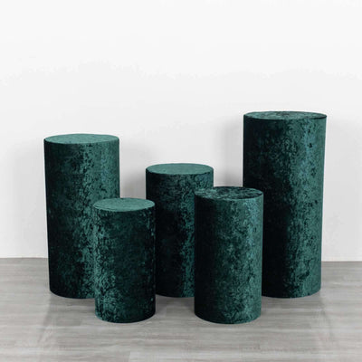 Set of five green velvet pedestals in varying heights on a plain backdrop.