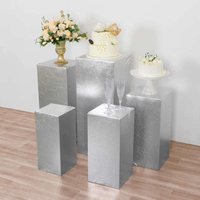Decorative silver display pedestals with floral arrangements and cakes.