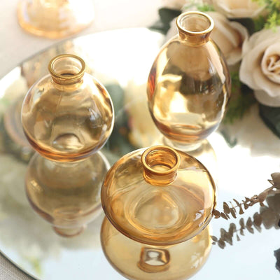 Set of three amber glass vases on a reflective surface.