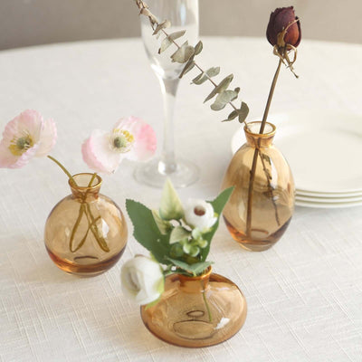Amber glass vases with flowers on a table setting.
