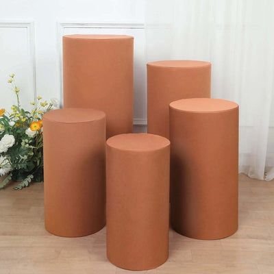 Set of five cylindrical brown pedestals in varying heights on a wooden floor.