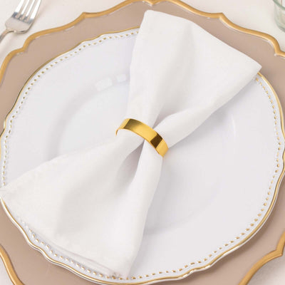 Elegant white napkin with gold napkin ring on a decorative plate.