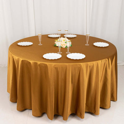 Round gold tablecloth with white plates and floral centerpiece.