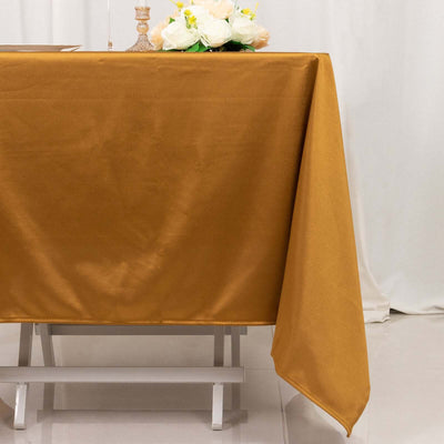 Gold tablecloth draped on a table with flowers in the background.