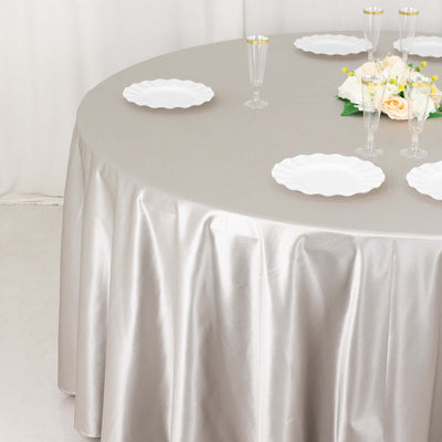 Elegant round table set with silver tablecloth, white plates, and floral centerpiece.