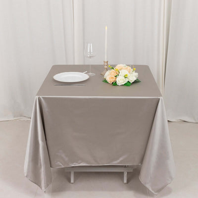 Elegant dining setup with a beige tablecloth, plate, glass, candle, and flowers.