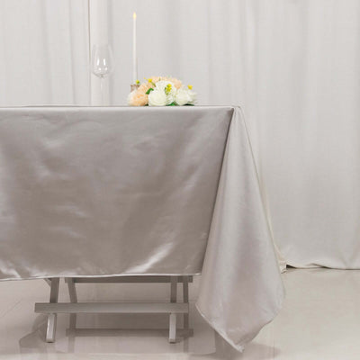 Elegant silver tablecloth draped over a wooden table with a candle and flowers.