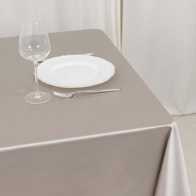 Elegant table setting with a glass, plate, and cutlery on a taupe tablecloth.