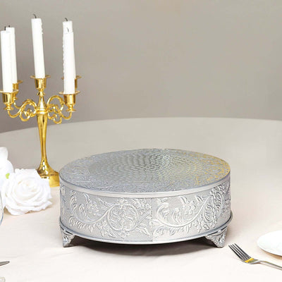 Silver embossed cake stand on a dining table with candles and flowers.