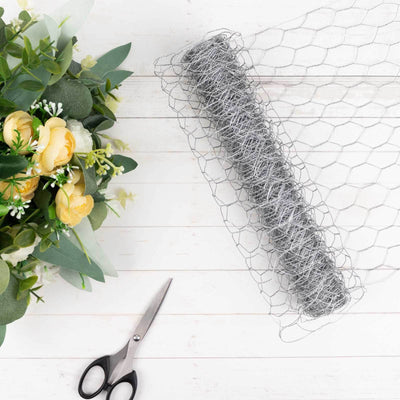 Wire mesh roll with scissors and artificial flowers on a wooden surface.