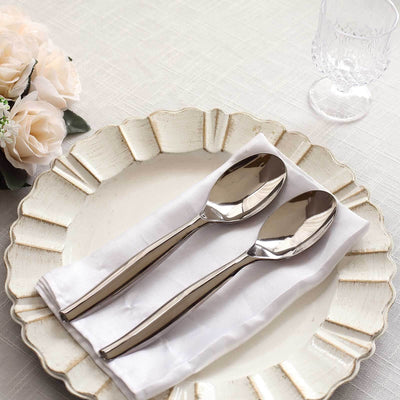 Elegant stainless steel serving spoons on a decorative plate with a napkin.