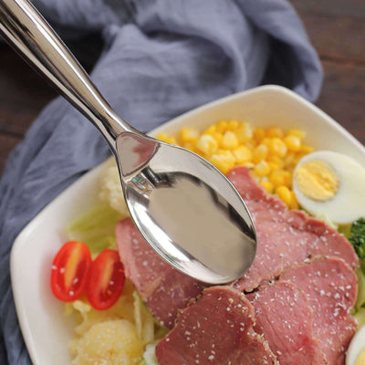 Silver serving spoon on a plate of salad with beef, corn, and cherry tomatoes.