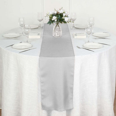 Gray table runner on a round table set for dining with floral centerpiece.