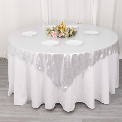 Round table with silver tablecloth and decorative centerpiece.