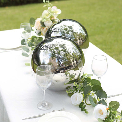 Decorative shiny spheres on a table with flowers and greenery in a garden setting.