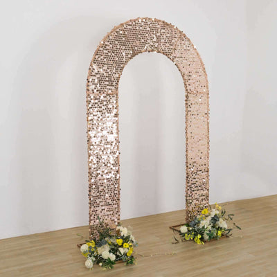 Rose gold sequin arch with floral arrangements at the base for events and celebrations.