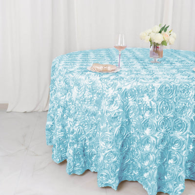 Textured turquoise tablecloth on a round table with a glass and flowers.