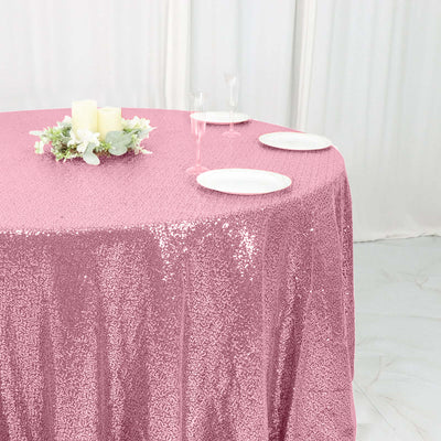 Pink sequin tablecloth draped over a round table with plates and candles.