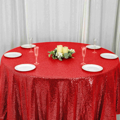 Red sequin tablecloth on round table set with plates and glasses for an elegant event.