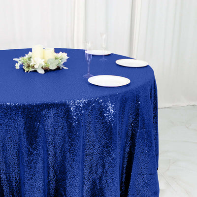 Blue sequin tablecloth draped over a round table with plates and floral centerpiece.