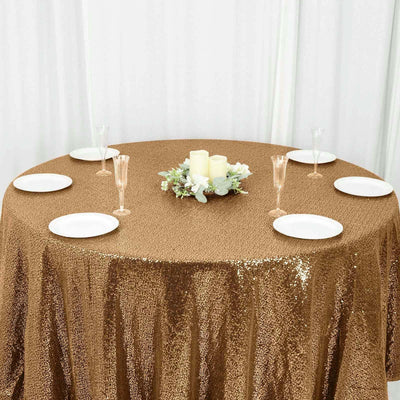 Gold sequin tablecloth on a round table set for dinner with floral centerpiece.