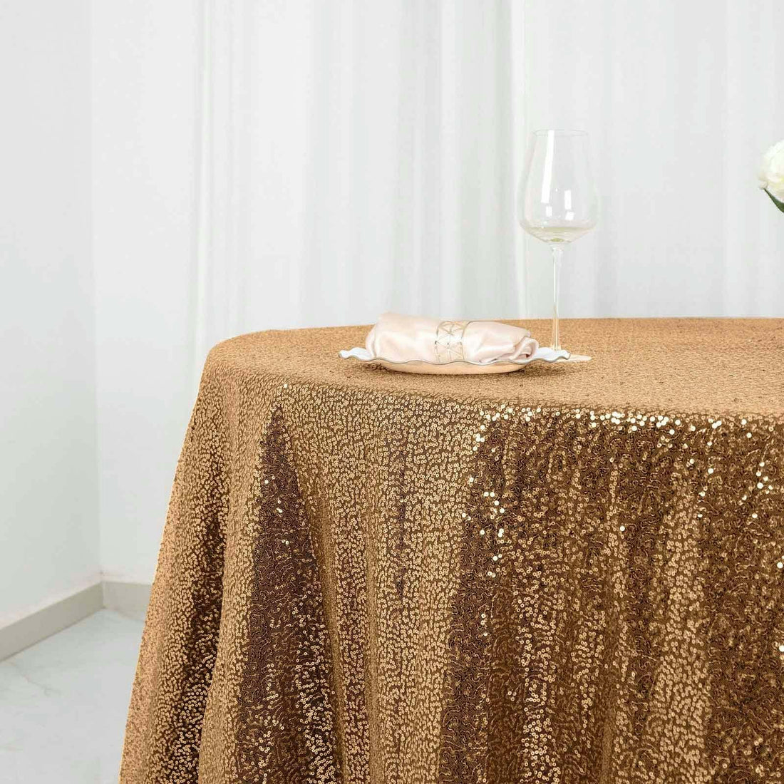 Gold sequin tablecloth with a glass and napkin on a table.