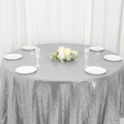 Elegant silver sequin tablecloth with decorative centerpiece and plates set for a gathering.