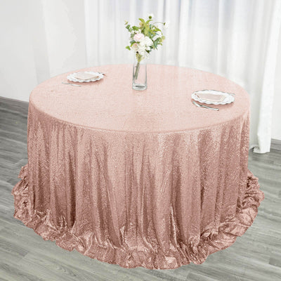 Rose gold sequin tablecloth draped over a round table with plates and flowers.