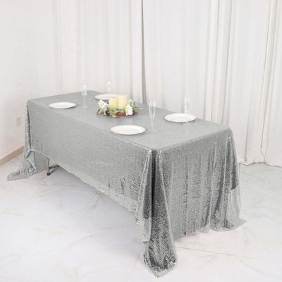 Silver sequin tablecloth draped over a rectangular dining table with plates and candles.